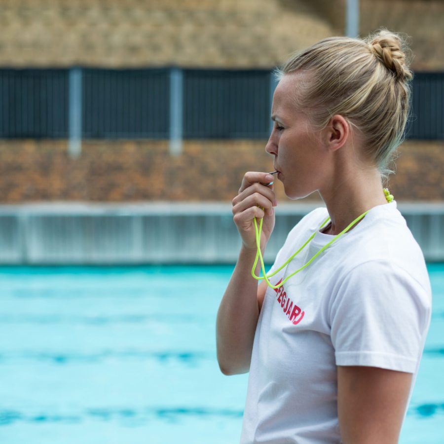 Side view of female lifeguard whistling at poolside